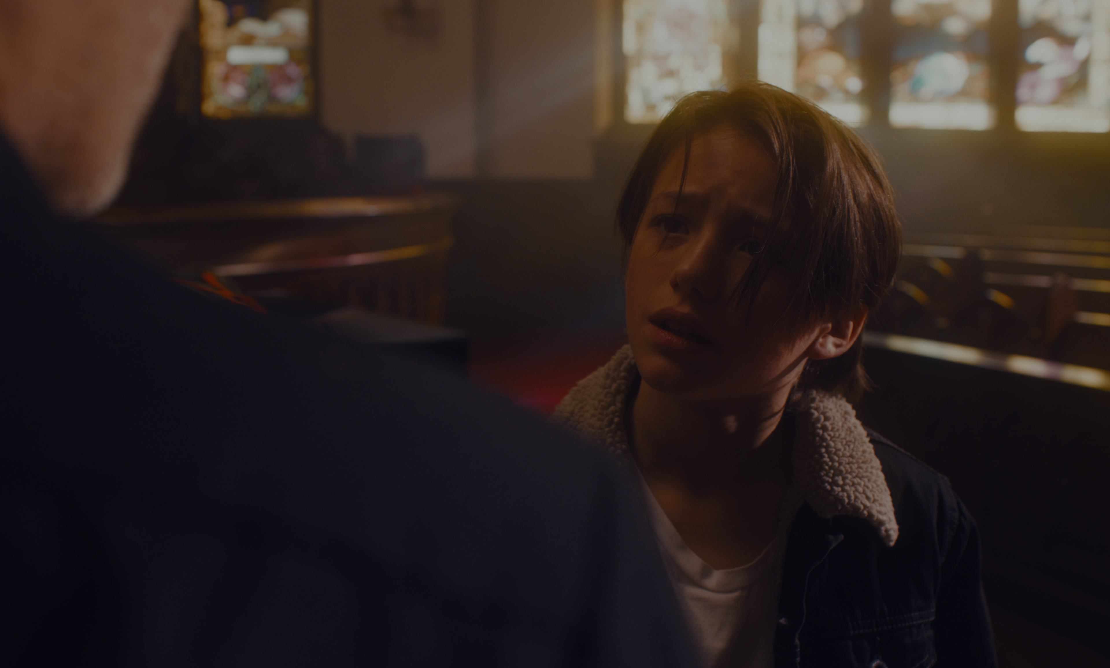 A young boy in a shearling-collared jacket looking up at a man inside the church